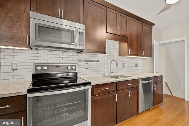kitchen with light stone countertops, a sink, stainless steel appliances, decorative backsplash, and light wood-type flooring
