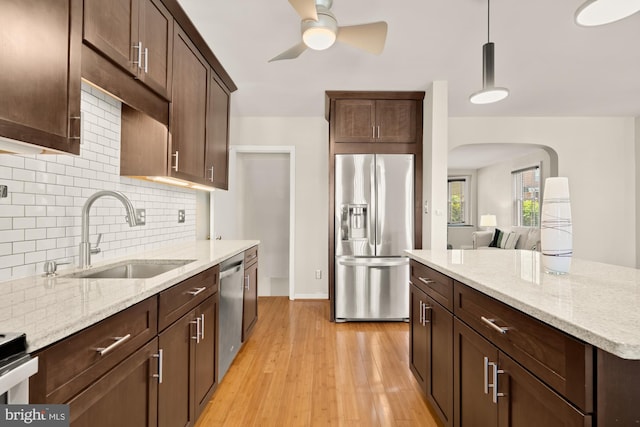 kitchen with a sink, light wood finished floors, arched walkways, stainless steel appliances, and tasteful backsplash