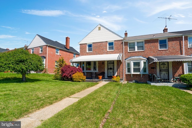 multi unit property with brick siding, a front lawn, covered porch, and a chimney