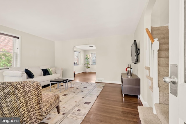 living area with arched walkways, visible vents, wood finished floors, and stairway