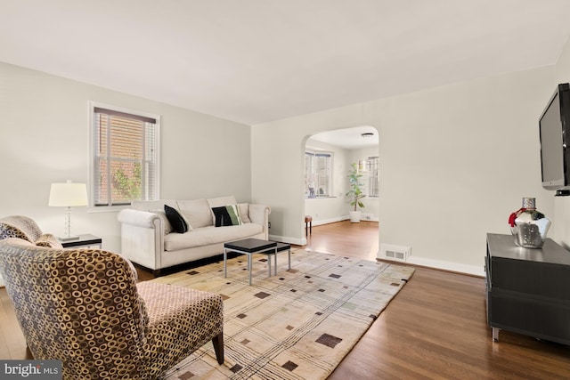 living area with arched walkways, plenty of natural light, wood finished floors, and visible vents