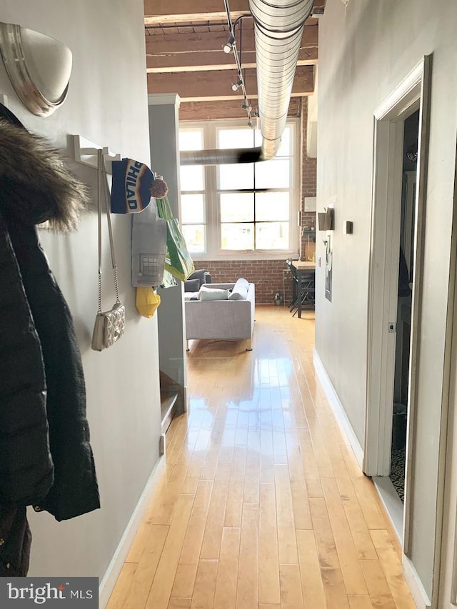 hallway featuring brick wall, baseboards, and light wood-type flooring