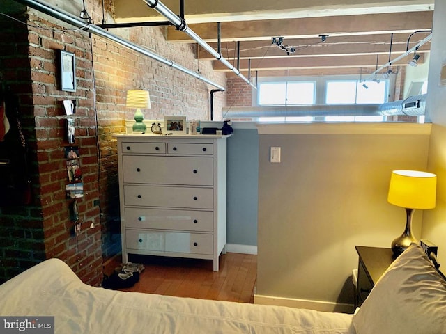 bedroom with baseboards, brick wall, and hardwood / wood-style floors