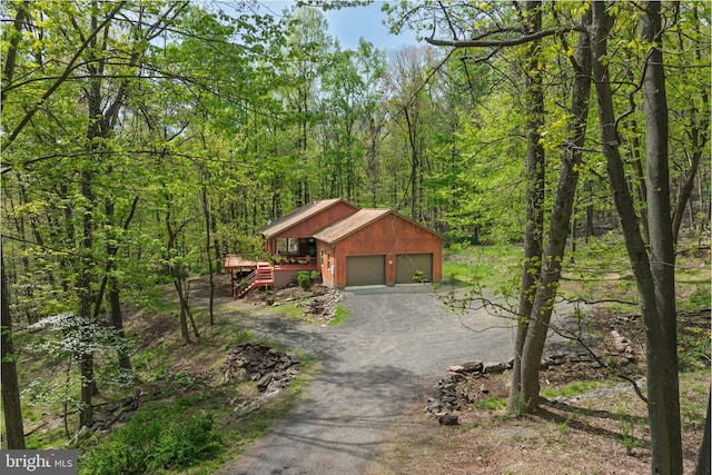 exterior space with a wooden deck, stairs, an attached garage, driveway, and a forest view