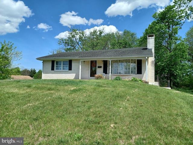 ranch-style home featuring a chimney, brick siding, and a front yard