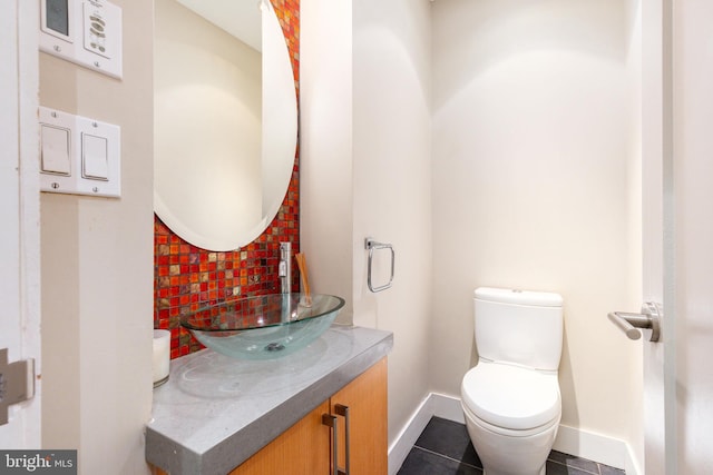 half bathroom featuring baseboards, tile patterned floors, vanity, and toilet