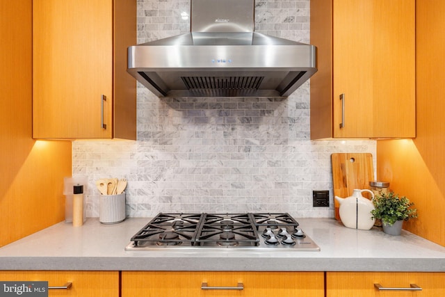 kitchen featuring wall chimney range hood, light countertops, decorative backsplash, and stainless steel gas stovetop