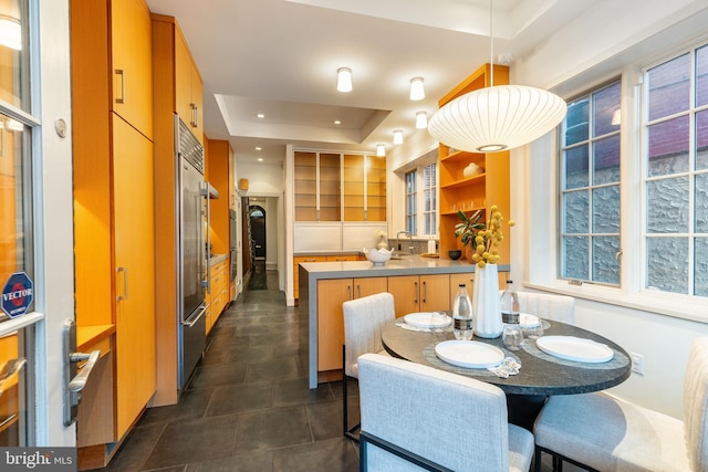 kitchen with brown cabinets, open shelves, a peninsula, a tray ceiling, and stainless steel built in refrigerator