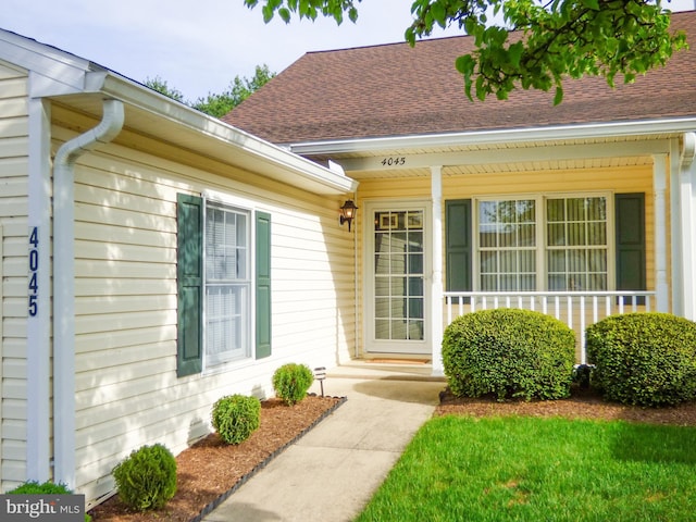 view of exterior entry featuring covered porch and a shingled roof