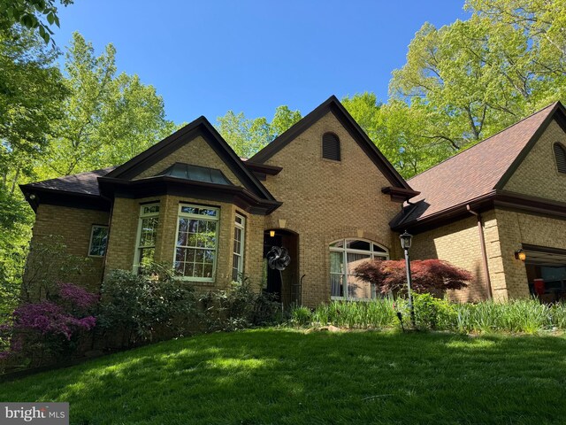 tudor-style house featuring a shingled roof, a front yard, and brick siding