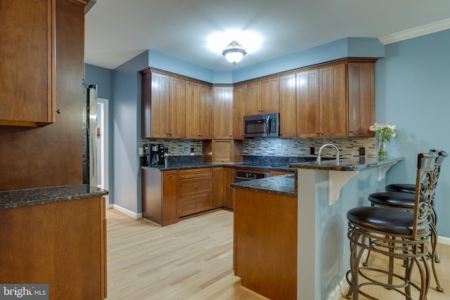 12868 Paddle Wheel Ct, Manassas, VA 20112 - kitchen with stainless steel microwave, light wood-style floors, a peninsula, a breakfast bar, and brown cabinetry