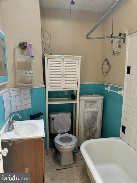 full bath featuring tile patterned flooring, vanity, toilet, a wainscoted wall, and a bath