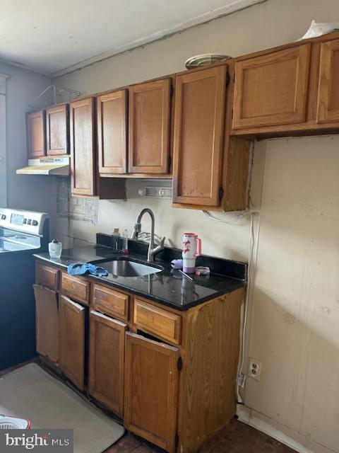 kitchen featuring brown cabinetry, electric range, dark countertops, under cabinet range hood, and a sink