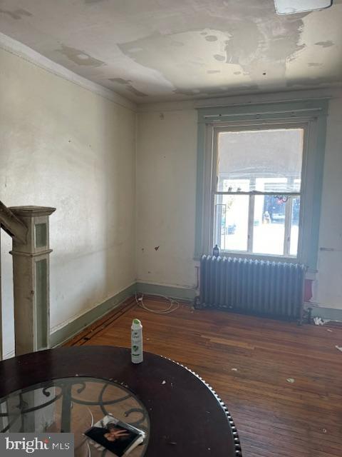 unfurnished living room with wood finished floors, baseboards, crown molding, and radiator heating unit