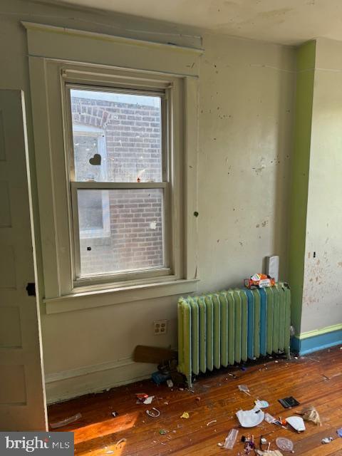 unfurnished room with radiator heating unit, baseboards, and hardwood / wood-style flooring