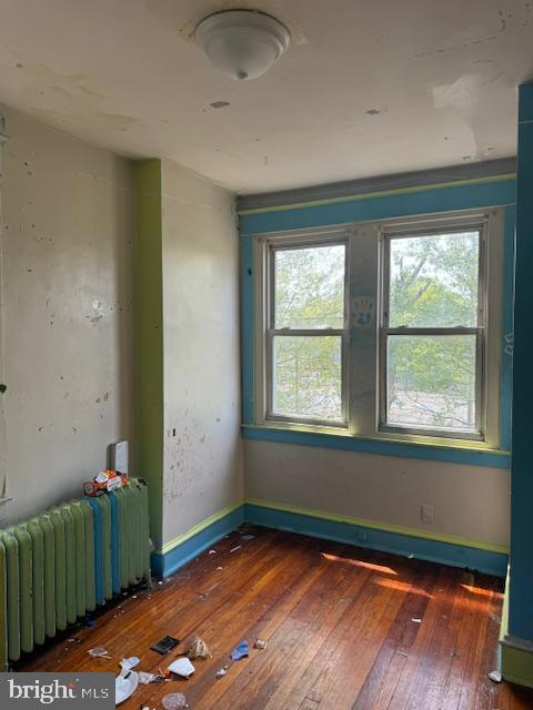 empty room with baseboards, radiator heating unit, and hardwood / wood-style floors