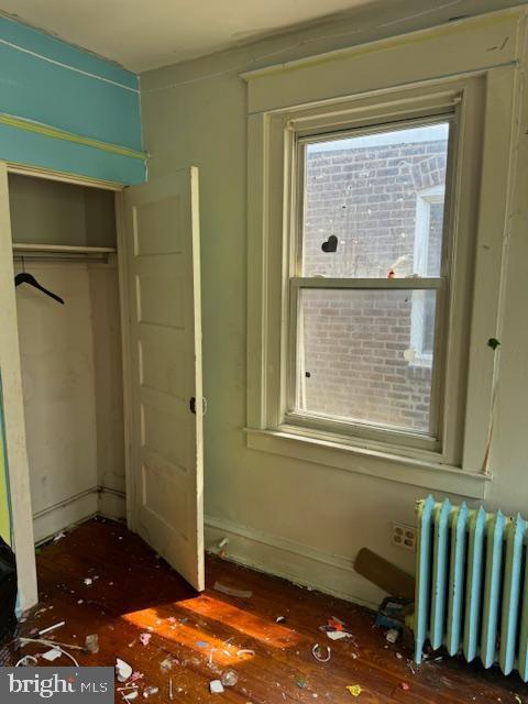 unfurnished bedroom with a closet, radiator, and wood finished floors