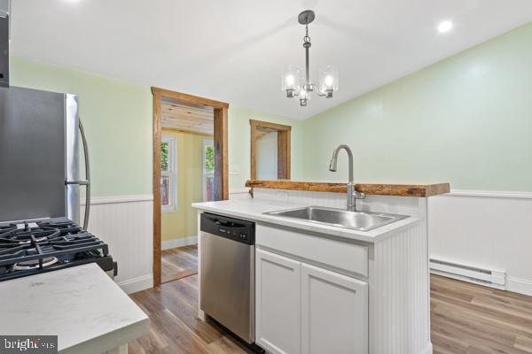 kitchen featuring appliances with stainless steel finishes, a sink, light countertops, white cabinets, and a baseboard heating unit