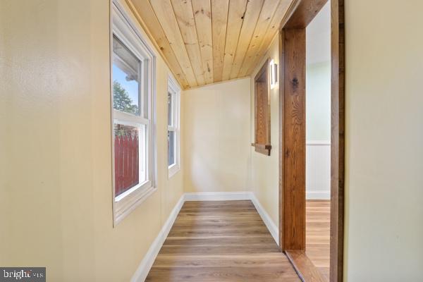 hall with baseboards, light wood-style flooring, and wood ceiling