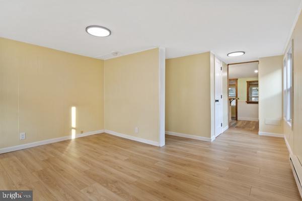 spare room featuring baseboards, a baseboard heating unit, and light wood finished floors