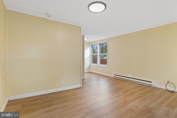 empty room featuring baseboards, a baseboard radiator, and wood finished floors