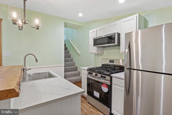kitchen with light wood-style floors, recessed lighting, white cabinets, a sink, and appliances with stainless steel finishes