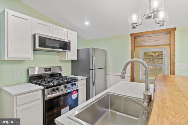 kitchen with white cabinetry, appliances with stainless steel finishes, a sink, and lofted ceiling