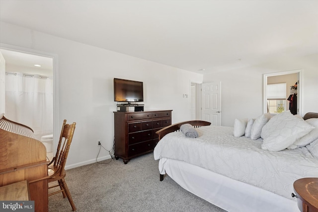 bedroom featuring a walk in closet, baseboards, a closet, ensuite bathroom, and light carpet