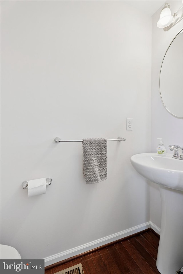 half bathroom with baseboards, wood finished floors, and toilet