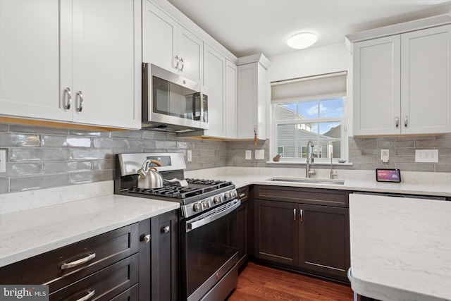 kitchen featuring decorative backsplash, white cabinets, light stone counters, a sink, and appliances with stainless steel finishes
