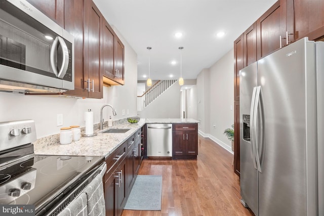 kitchen with light stone countertops, a sink, a peninsula, light wood-style floors, and stainless steel appliances