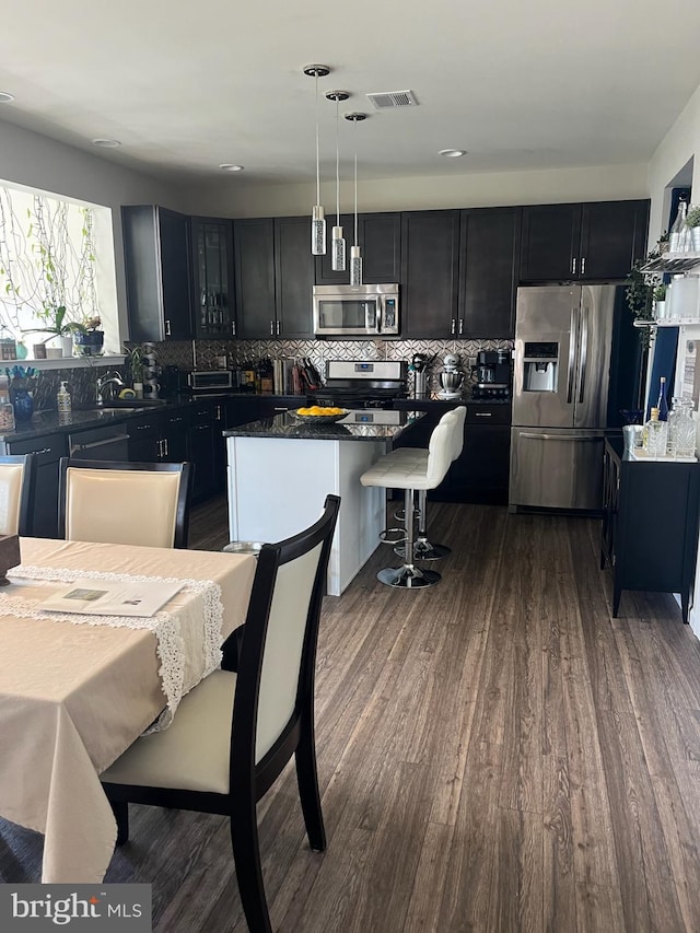kitchen with dark cabinets, dark wood finished floors, stainless steel appliances, tasteful backsplash, and a kitchen island