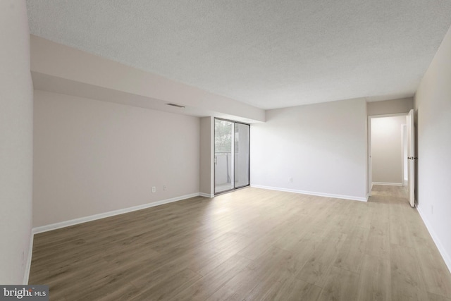unfurnished room featuring baseboards, light wood finished floors, a textured ceiling, and visible vents