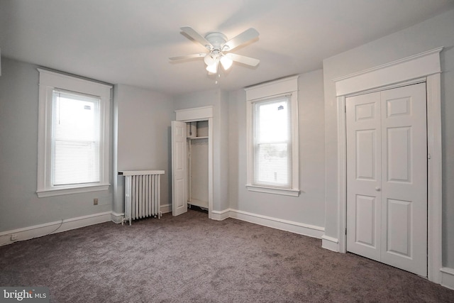 unfurnished bedroom with multiple closets, radiator heating unit, dark colored carpet, a ceiling fan, and baseboards