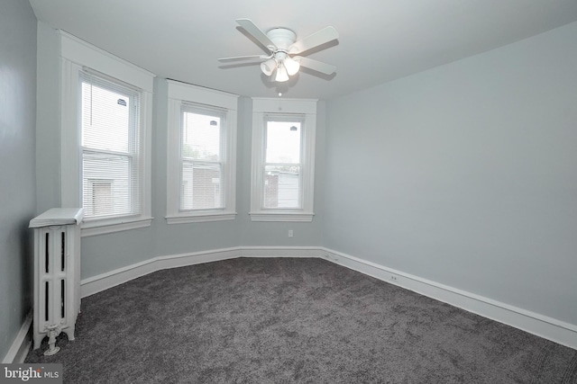 empty room with baseboards, ceiling fan, dark carpet, and radiator