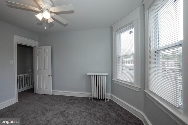 unfurnished bedroom with a ceiling fan, baseboards, radiator heating unit, and dark colored carpet