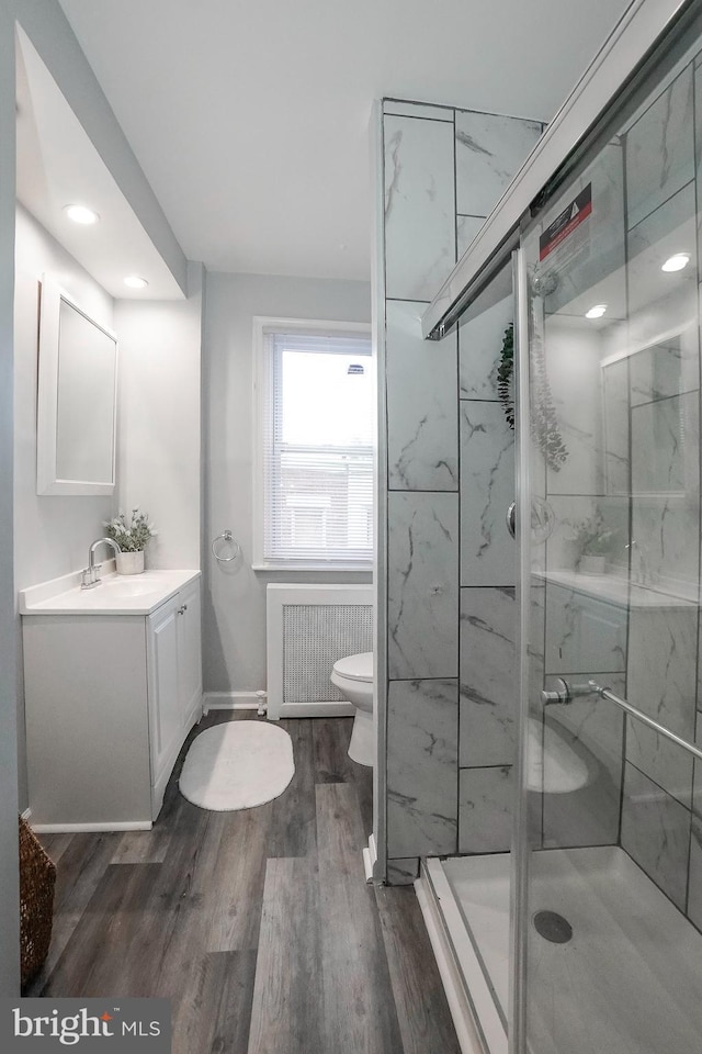 full bathroom featuring vanity, wood finished floors, toilet, radiator heating unit, and a shower stall