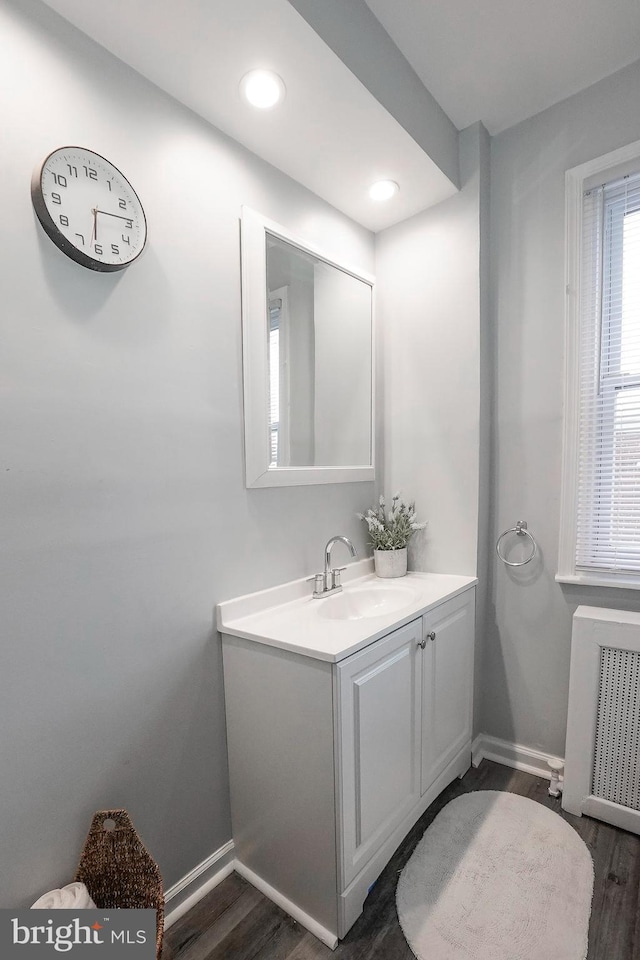 bathroom featuring wood finished floors, baseboards, vanity, radiator, and recessed lighting