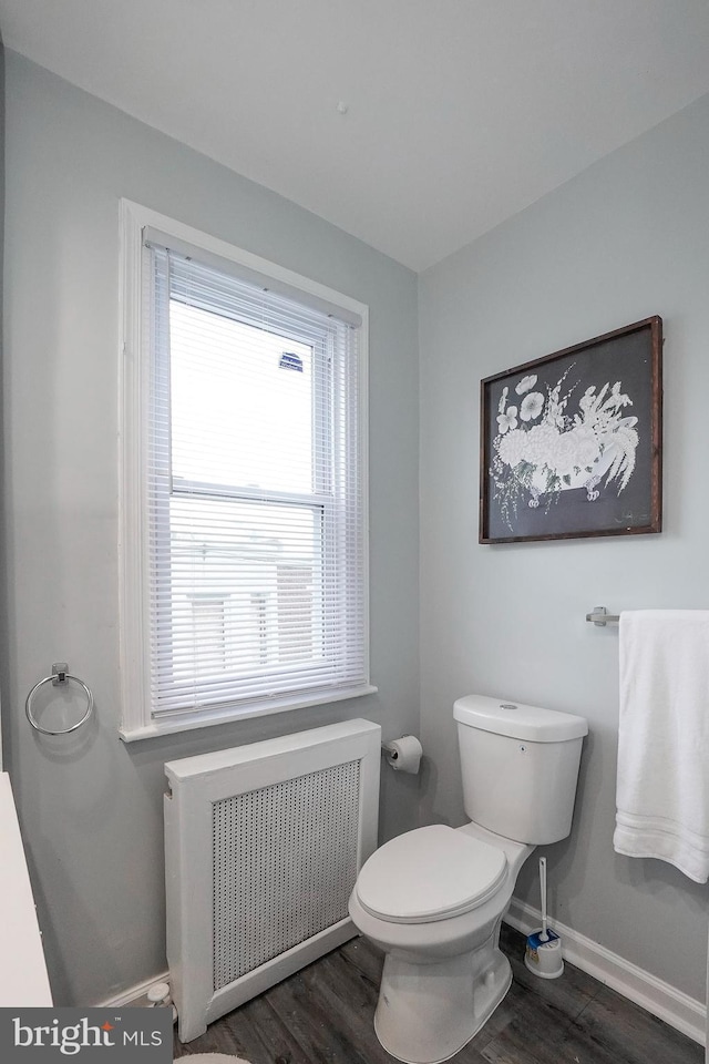 bathroom with radiator heating unit, baseboards, toilet, and wood finished floors