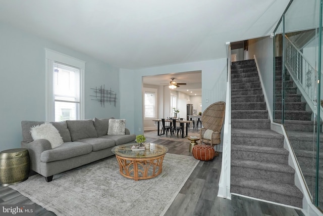 living area with baseboards, ceiling fan, wood finished floors, and stairway