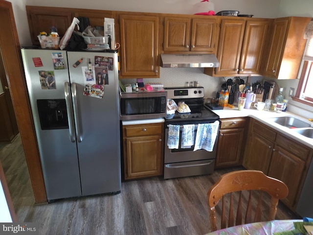 kitchen with brown cabinetry, extractor fan, light countertops, dark wood finished floors, and appliances with stainless steel finishes