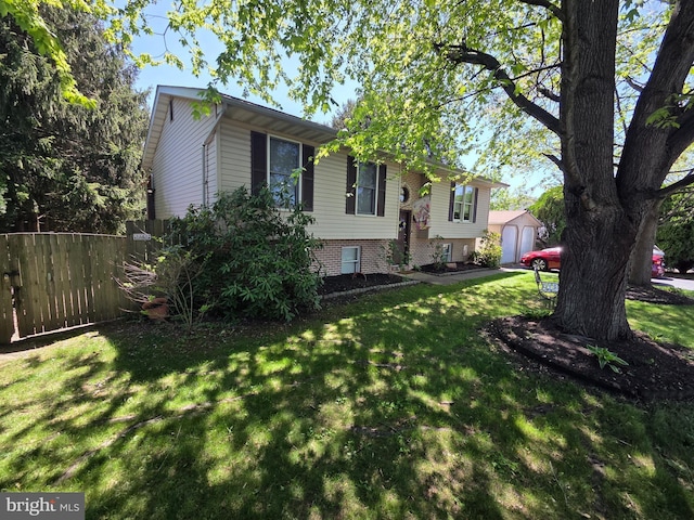 bi-level home with a detached garage, fence, an outbuilding, and a front lawn