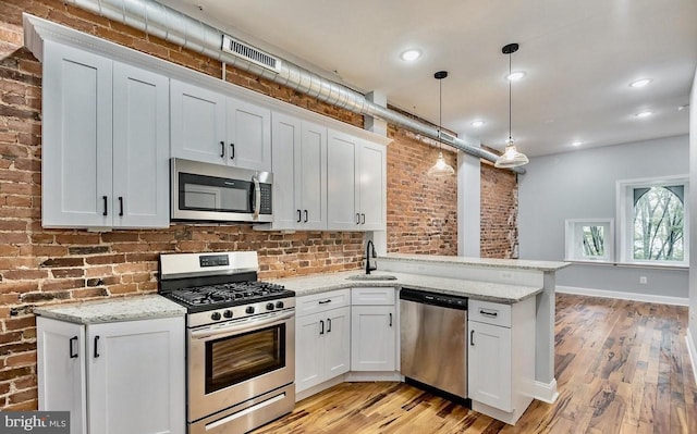 kitchen with visible vents, a peninsula, light wood-style floors, a sink, and appliances with stainless steel finishes