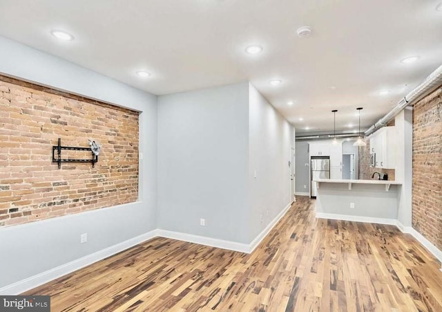 unfurnished living room featuring recessed lighting, baseboards, light wood-type flooring, and brick wall