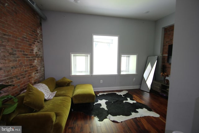 living area featuring baseboards, wood finished floors, and brick wall