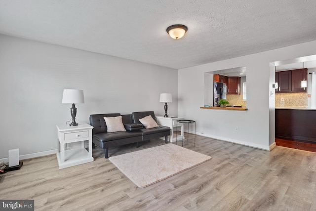 living area featuring light wood-type flooring, baseboards, and a textured ceiling