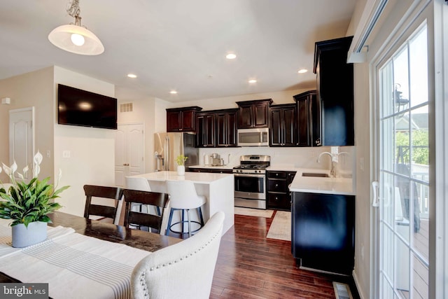 kitchen featuring stainless steel appliances, a sink, light countertops, dark wood finished floors, and a center island