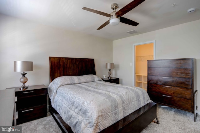 bedroom with light carpet, ceiling fan, and a walk in closet
