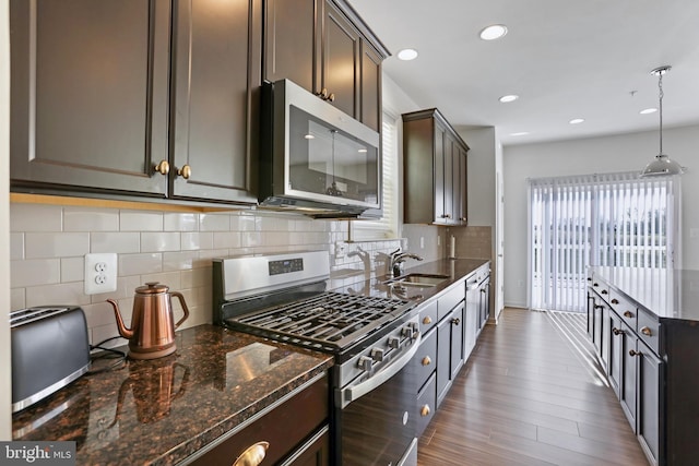 kitchen featuring appliances with stainless steel finishes, a sink, dark stone countertops, decorative backsplash, and dark wood-type flooring
