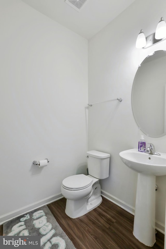 bathroom featuring a sink, toilet, baseboards, wood finished floors, and visible vents